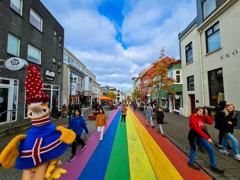 visitare Reyjavik Baba si fa fotografare davanti alla famosa passeggiata arcobaleno di Reykjavik mentre le persone che affollano la via la guardano incuriosite